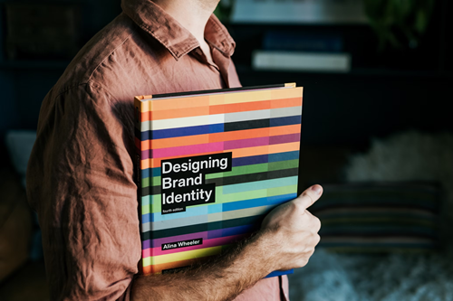 Person holding the book Designing Brand Identity by Alina Wheeler.
