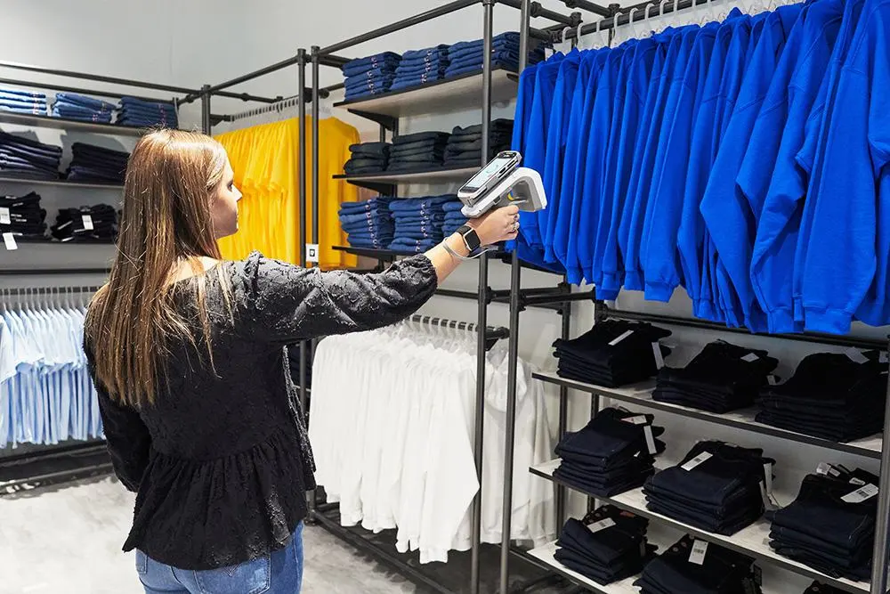 Retail employee using a handheld RFID reader to scan clothing on store racks for fast inventory management, stock tracking, and retail asset visibility.